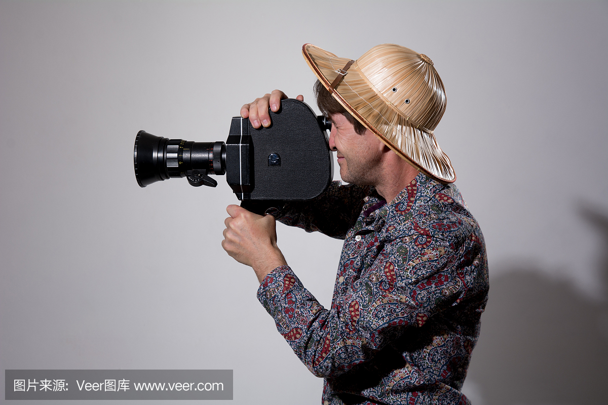 一个戴着草帽的男人,灰色的背景上放着一台旧的电影摄像机